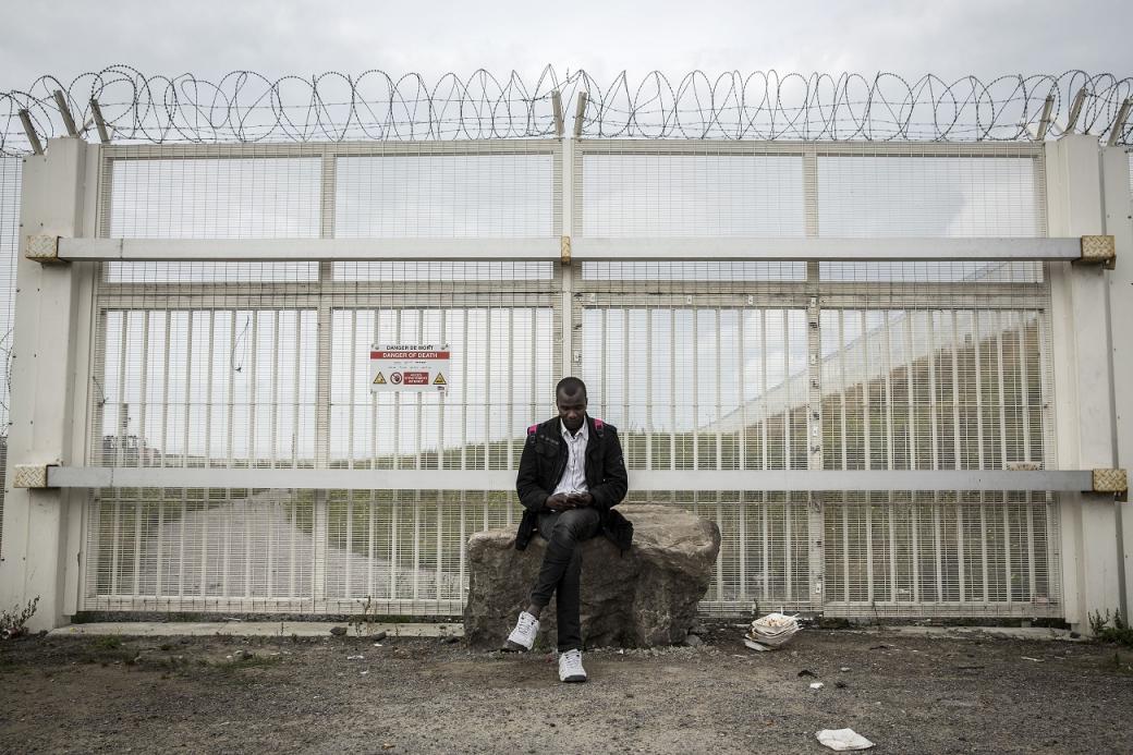 Un migrante sudanés sentado junto a una de las muchas alambradas que rodean el puerto de Calais. / Olmo Calvo