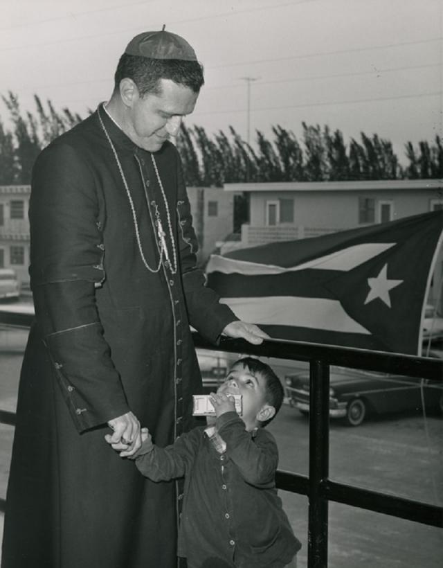 El obispo auxiliar de La Habana Eduardo Boza Masvidal, con un refugiado cubano de tres años (1963). /Cortesía del archivo de la Barry University - Special Collections