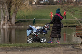 <p>Una mujer joven pasea a un bebé por un parque.</p>