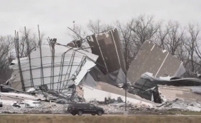 <p>Un coche pasa junto a restos de una nave destruida por el tornado en Edwardsville (Illinois, Estados Unidos).</p>