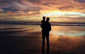 <p>Un hombre contempla el atardecer con su hijo en brazos. </p>