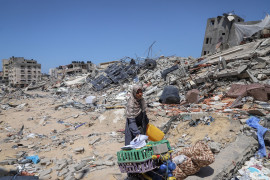 <p>Una mujer gazatí camina con algunos enseres entre los escombros. / <strong>Mohamed Hajjar</strong></p>