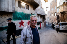 <p>En el barrio kurdo de Damasco, Rukn al-Din, un hombre posa junto a pintadas de la bandera de la revolución siria y la bandera palestina. / <strong>S.M.</strong></p>