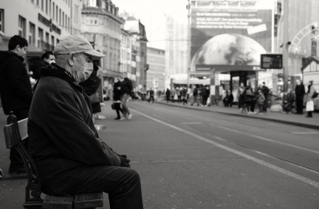 <p>Un hombre mayor sentado en un banco en la calle con la mascarilla puesta.</p>