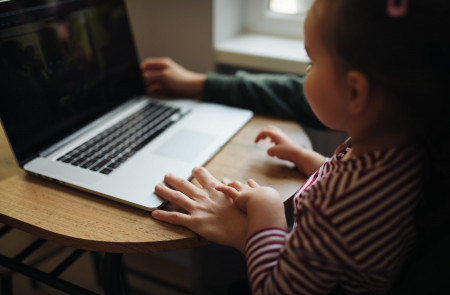 <p>Una niña mira el ordenador mientras su madre trabaja desde casa.</p>