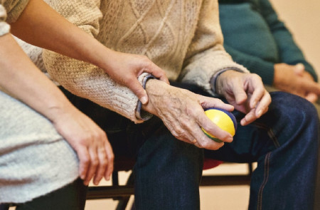 <p>Un anciano sostiene una pelota junto a una persona cuidadora.</p>