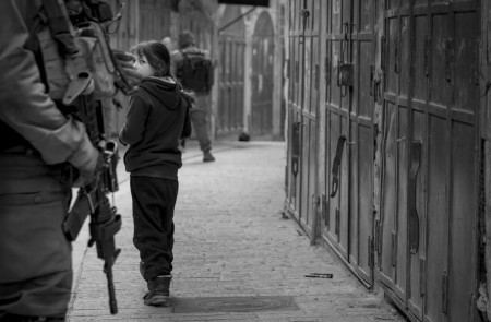 <p>Una niña palestina mira a un militar israelí de guardia en Cisjordania. <strong>/ Ariel Feldman </strong></p>