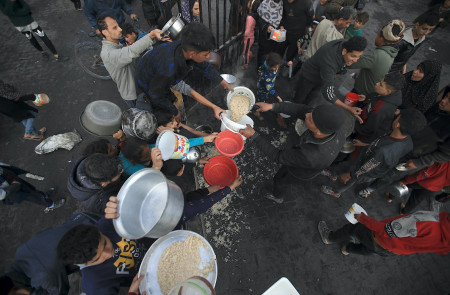 <p>Un grupo de hombres gazatíes se afanan por conseguir algo de comida durante el reparto. / <strong>Mahmoud Mushtaha</strong></p>