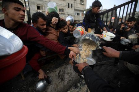 <p>Un grupo de hombres gazatíes se afanan por conseguir algo de comida durante el reparto. / <strong>Mahmoud Mushtaha</strong></p>