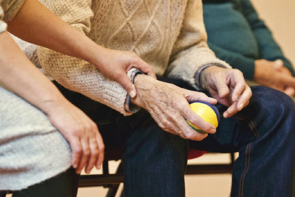 <p>Un anciano sostiene una pelota junto a una persona cuidadora.</p>