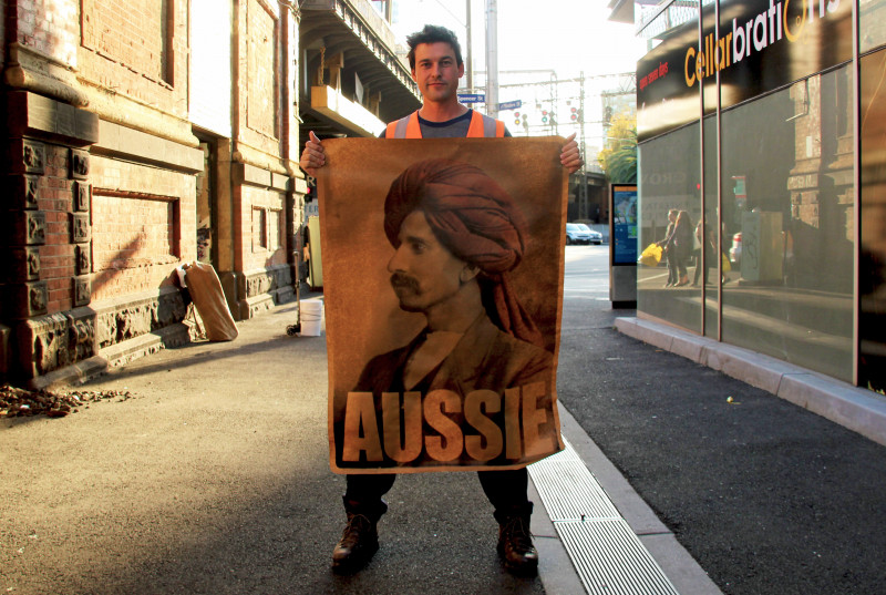 <p>Peter Drew posa junto a uno de los carteles con los que está empapelando Australia.</p>