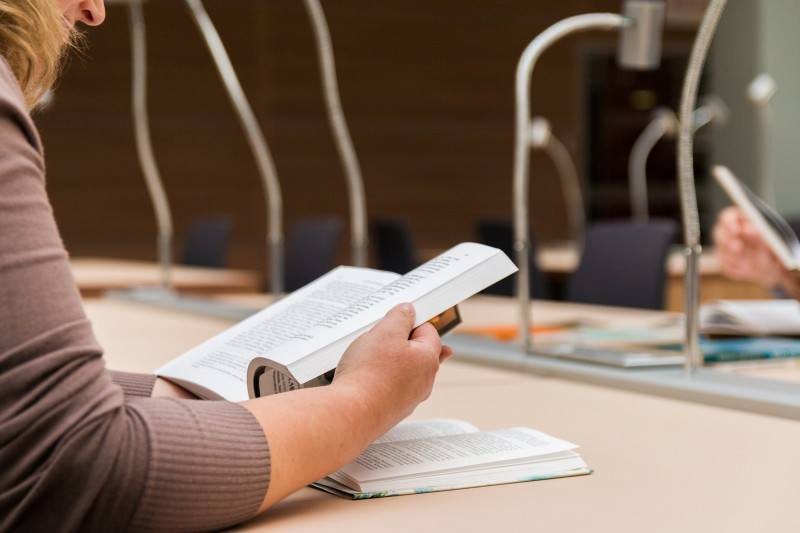 <p>Una persona lee en una biblioteca.</p>