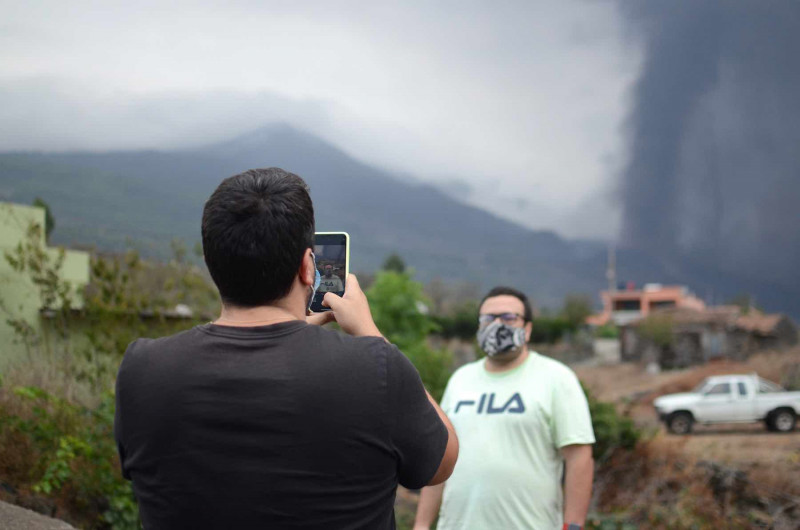 <p>Dos vecinos de La Palma se toman fotos con el volcán de fondo.</p>