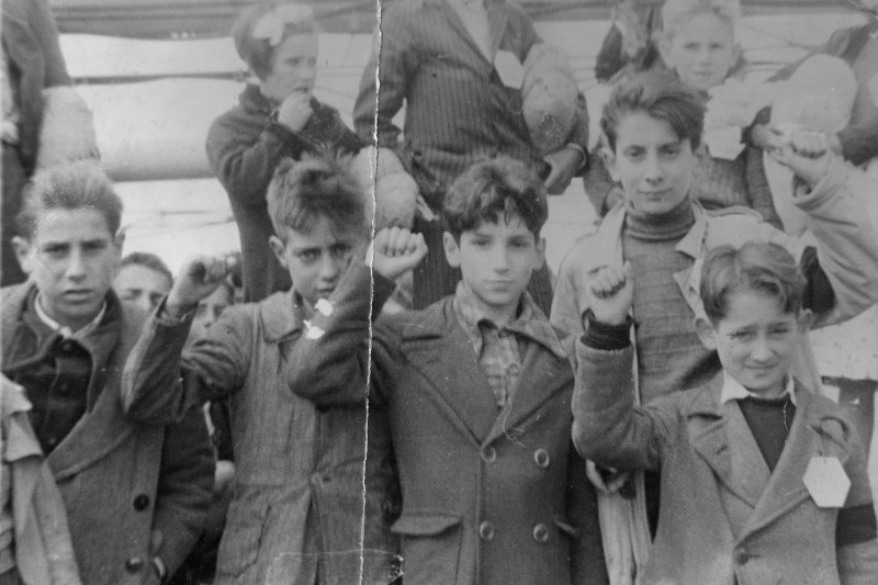 <p>Niños preparándose para la evacuación de España, durante la Guerra Civil, algunos haciendo el saludo republicano.</p>