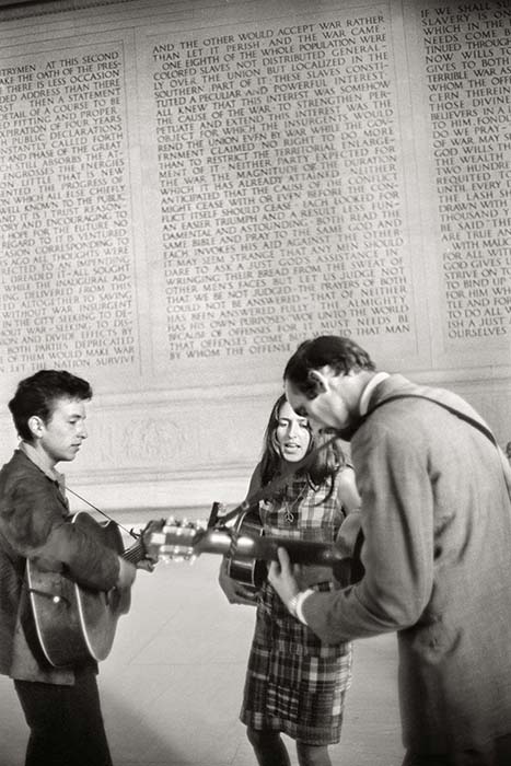Joan Baez, Bob Dylan y Pete Seeger se preparan para actuar con el texto de la constitución americana de 1776 de telón de fondo.