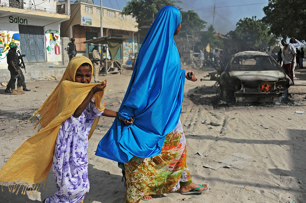 <p>Madre e hija pasan cerca de los restos de un coche bomba que ha matado a una persona y herido a otra. Wardhigley District, sur de Mogadisho,  27 de febrero de 2015. © Mohamed Abdiwahab / AFP.</p>