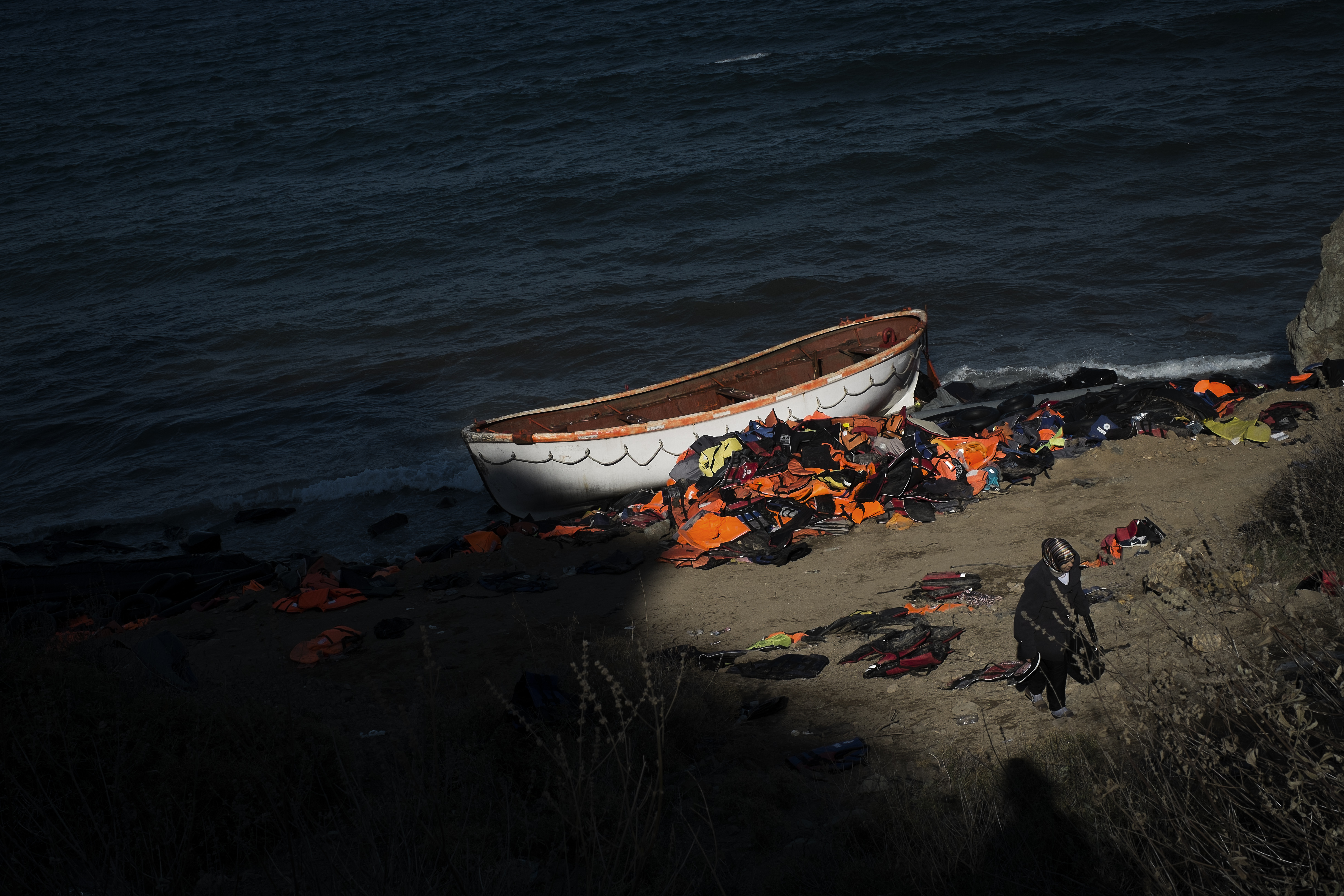 <p>Una mujer camina por la playa tras llegar en barca desde Turquía. A sus espaldas se amontona una montaña de chalecos salvavidas, muchos de ellos falsos.</p>