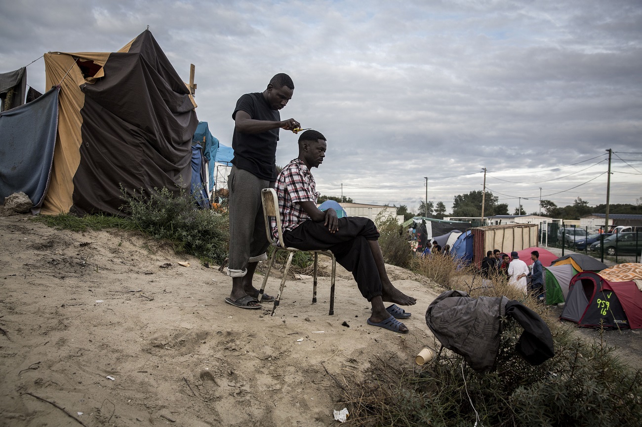 <p>Un migrante sudanés le corta el pelo a otro en una de las dunas donde se asienta la <em>jungla.</em> </p>