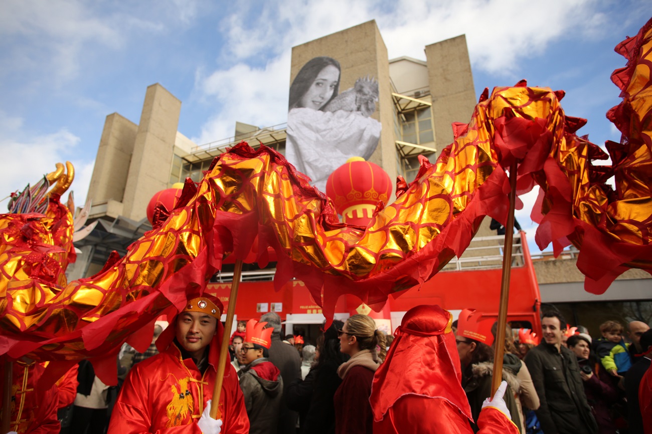 <p>La cabalgata del Año Nuevo chino desfila ante la junta municipal de distrito de Usera, donde cuelga el fotomural de Esther López portando el gallo rojo de fuego.</p>