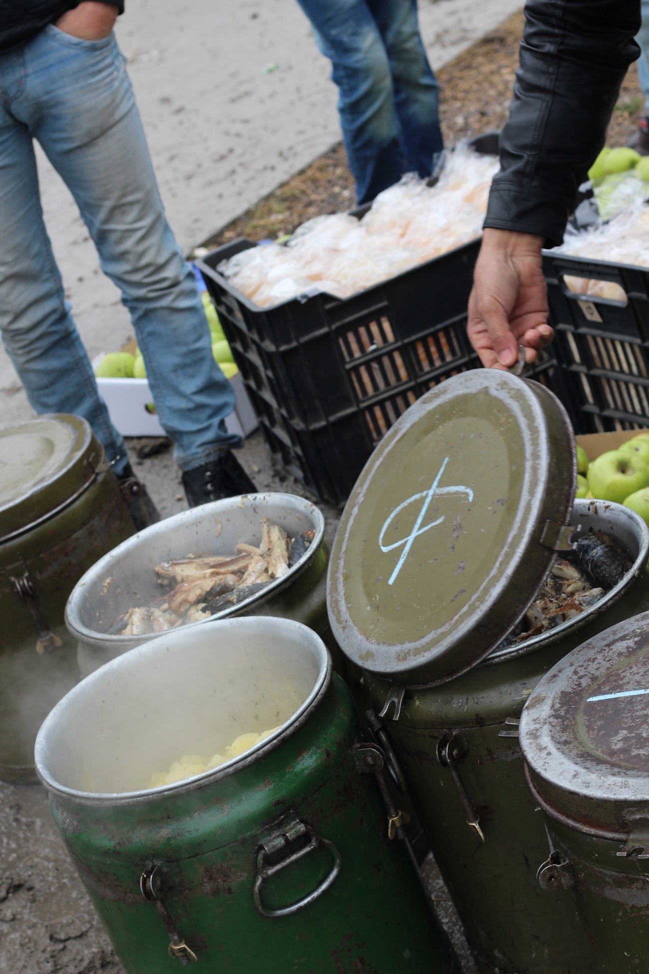 <p>Unos hombres muestran el contenido de los gastados bidones metálicos en los que se transporta la comida: pescado, patatas, manzanas y pan. </p>