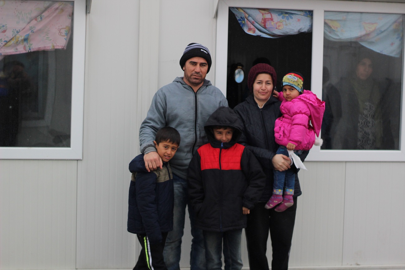 <p>Ali y Amina Ramadan posan con sus hijos delante del barracón donde viven. Antes de huir hacia Europa, el joven matrimonio ejercía como maestros de escuela en Hasaka (Kurdistán sirio).</p>