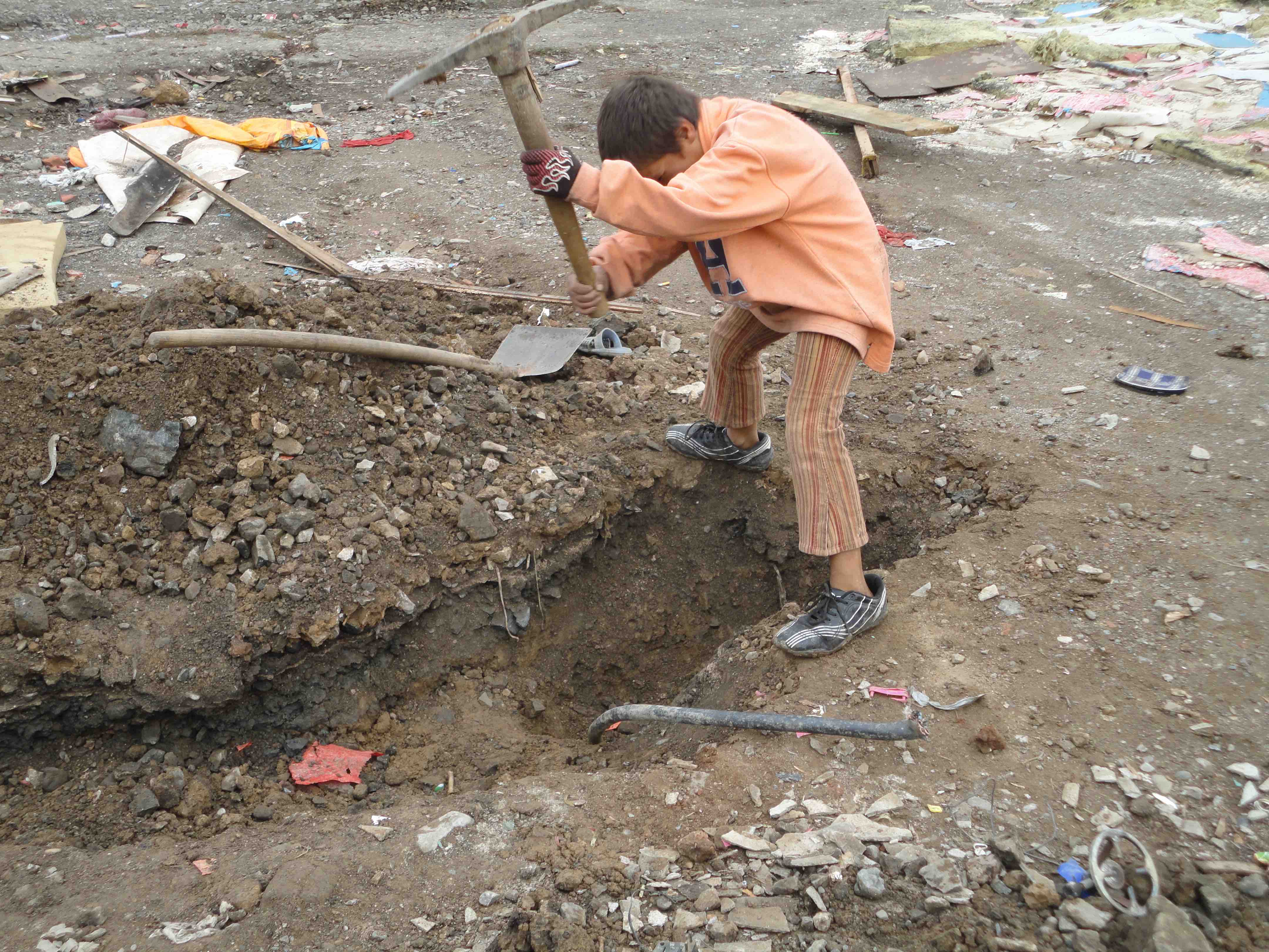 <p>Un niño pica en el suelo para poder extraer el cableado eléctrico del campo de Cesmin Lug.</p>